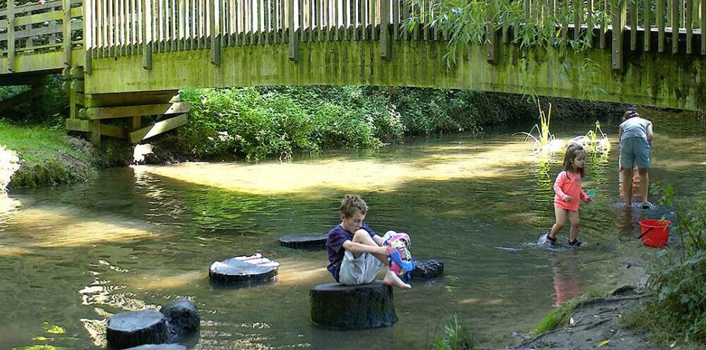 Children playing and around water with a wooden bridge above them. For things to do and outdoor adventures at Lullingstone Country Park in Eynsford in Sevenoaks in Kent